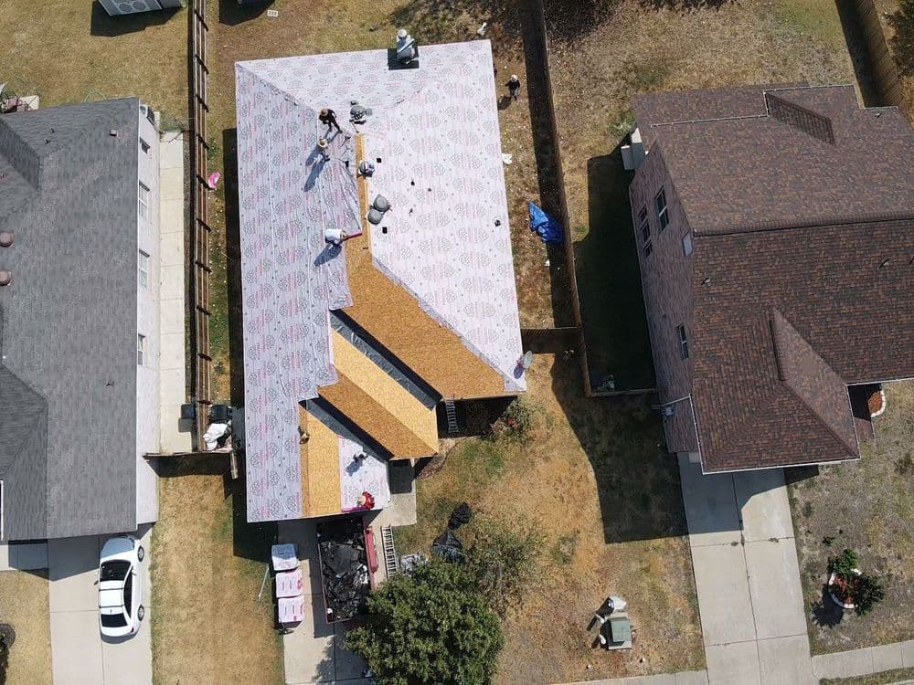 Aerial view of a residential roof installation with workers and materials visible.
