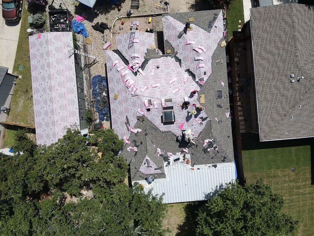 Aerial view of a residential roof under repair with roofing materials spread across.