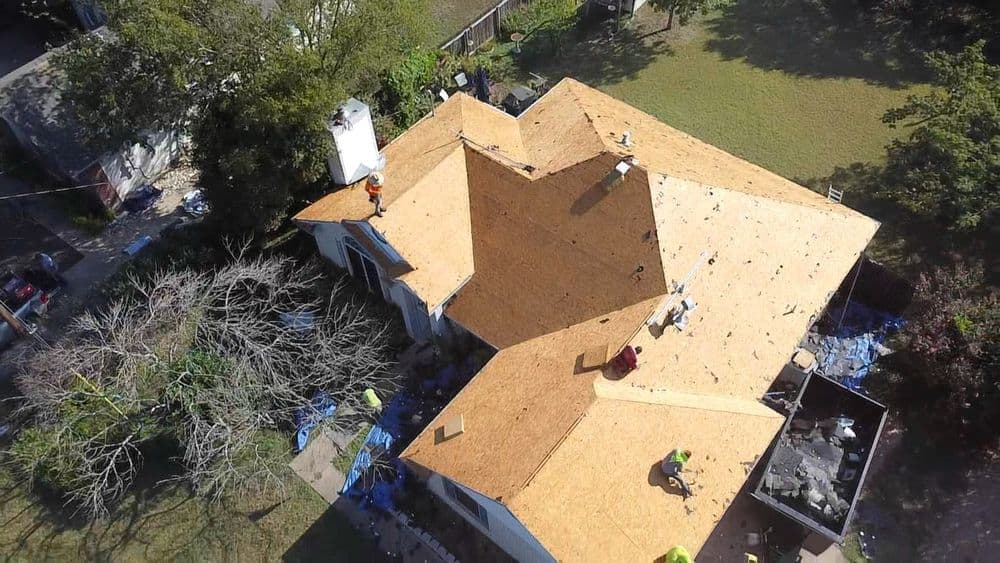 Aerial view of a house under roof restoration with workers installing new shingles.