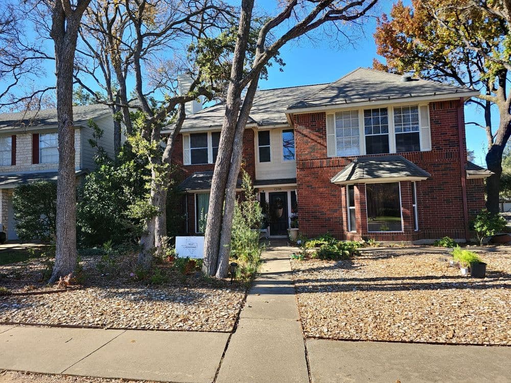 Two-story red brick house with a landscaped yard and tree-lined walkway.