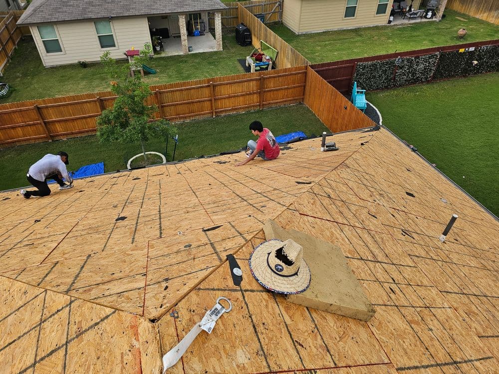 Workers installing a new roof on a house, featuring plywood sheathing and tools on the roof.