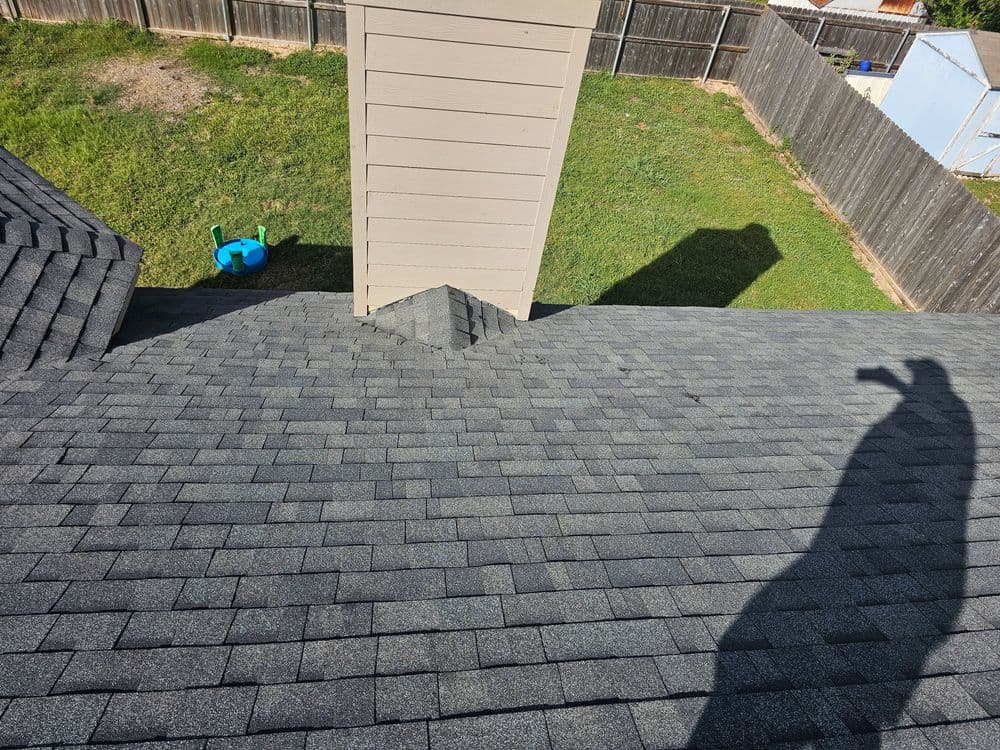 Aerial view of a gray shingle roof with a chimney and grassy backyard.